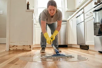 Femme utilisant un balai lave-sol trop humide sur un parquet en chêne, causant des dégâts liés à l'excès d'eau